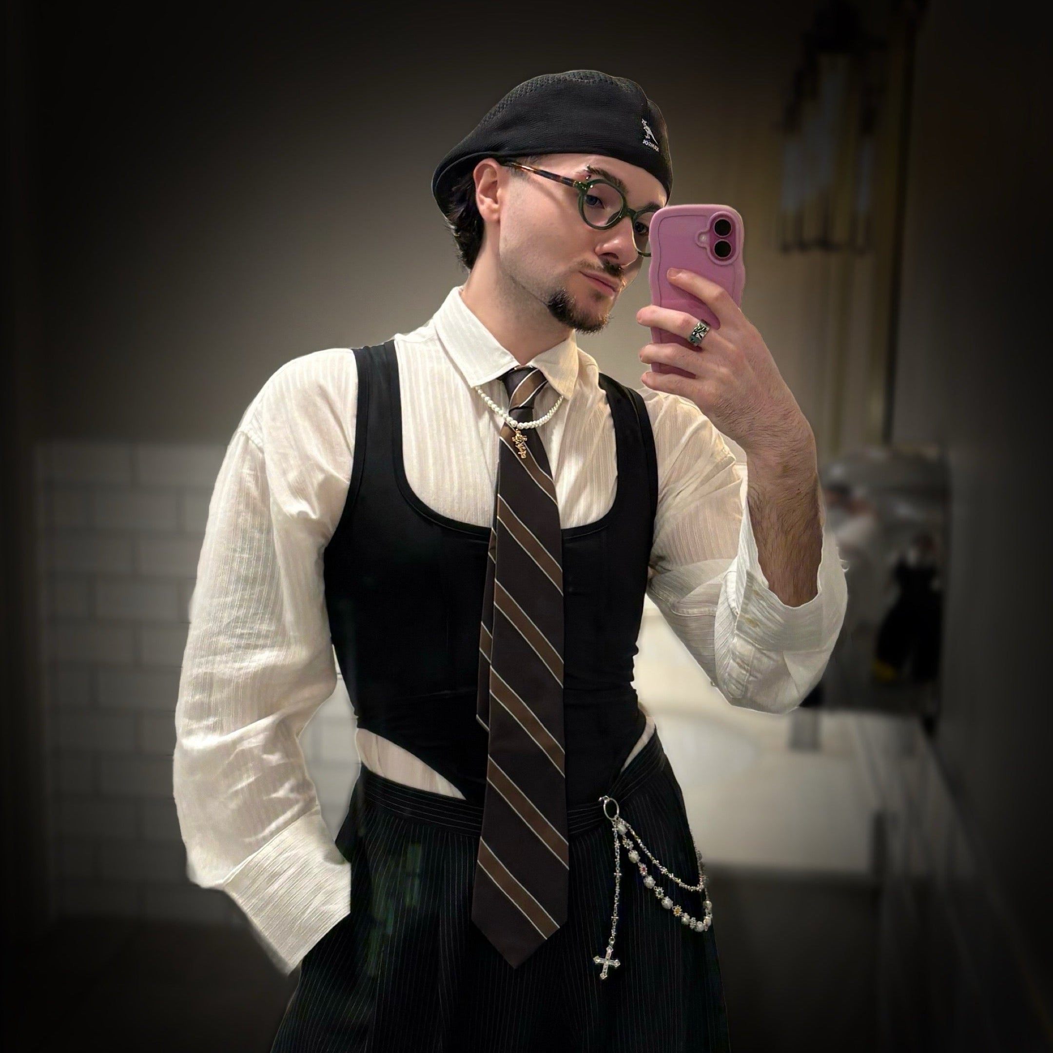 Person taking a mirror selfie wearing a white shirt, black vest, and striped tie.